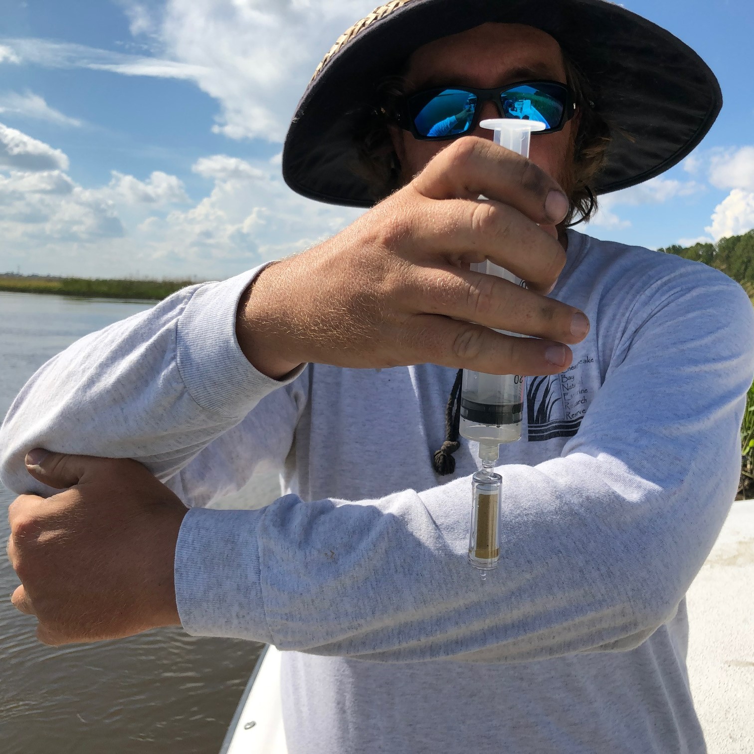 Researcher in boat holding up sample in container near marshy shoreline